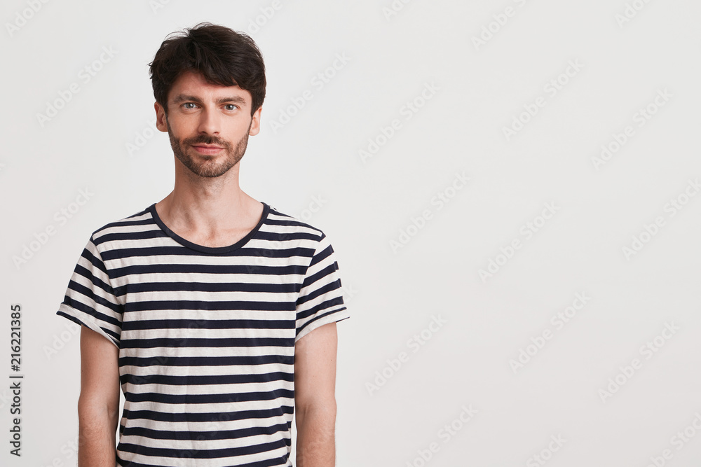 Closeup of happy attractive young man with bristle wears striped t shirt feels confident and looks directly in camera isolated over white background Closeup of happy attractive young man with bristle wears striped t shirt feels confident and looks directly in camera isolated over white background