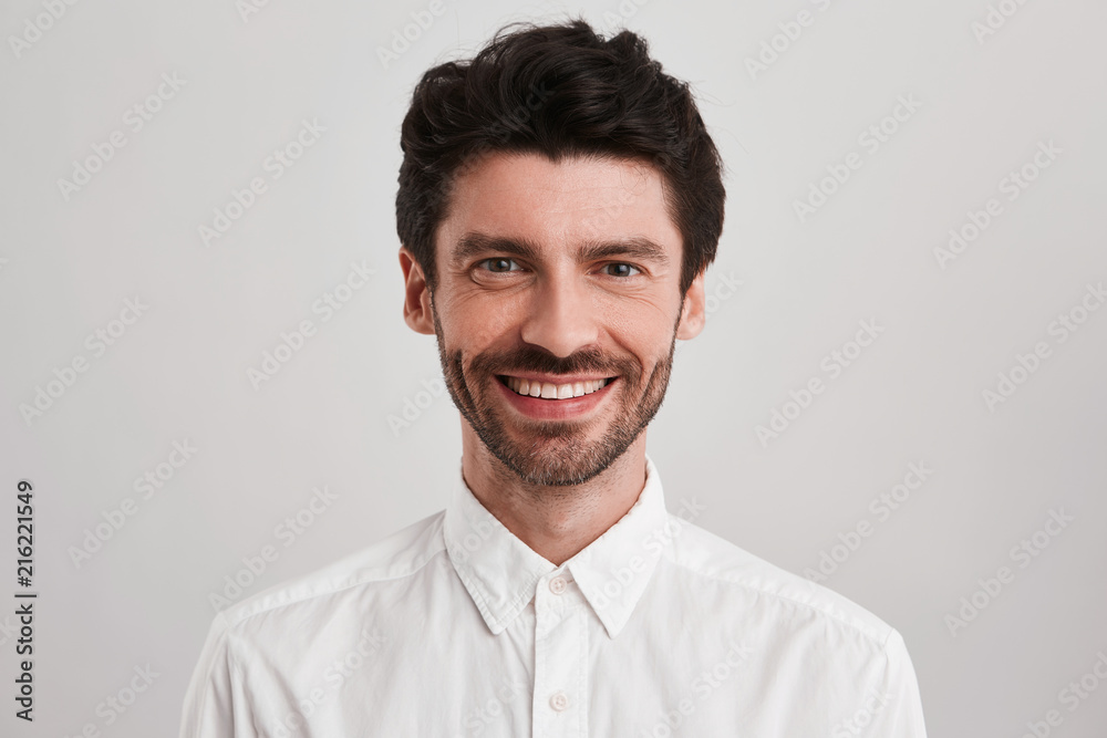 Unshaven confident smiling male, dressed casual white shirt looks directly into camera and feels happy about his job. Portrait of stylish handsome guy Unshaven confident smiling male, dressed casual white shirt looks directly into camera and feels happy about his job. Portrait of stylish handsome guy