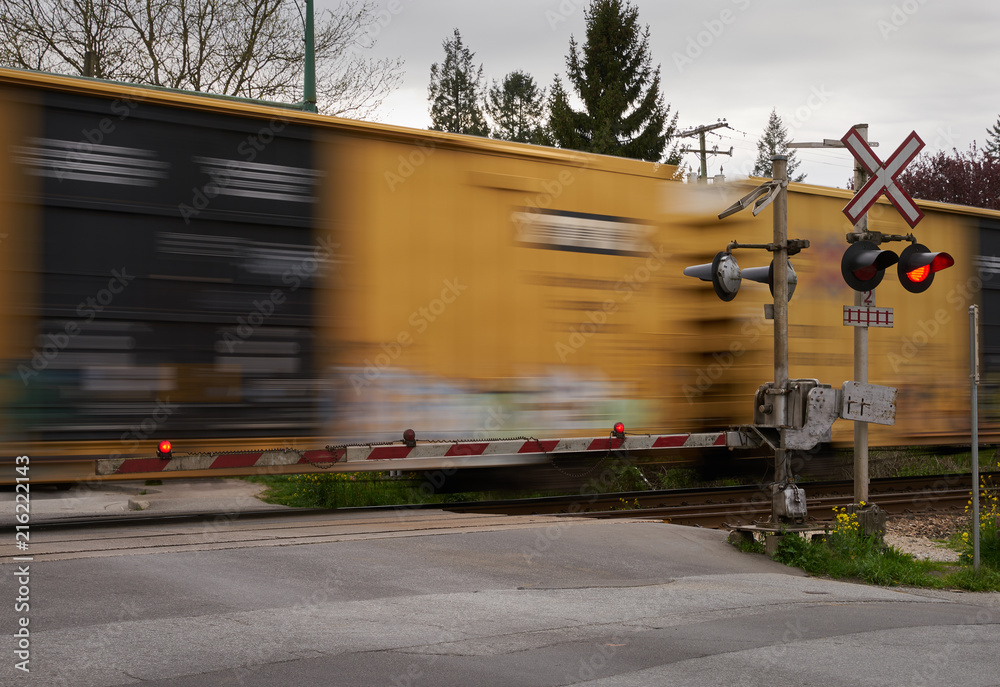 Naklejka premium Street Level Railway Crossing. A train passes a level train crossing with the crossing arms down and lights flashing.