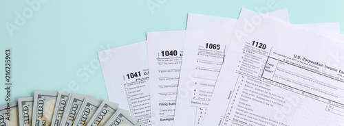 Tax forms lies near hundred dollar bills and blue pen on a light blue background. Income tax return