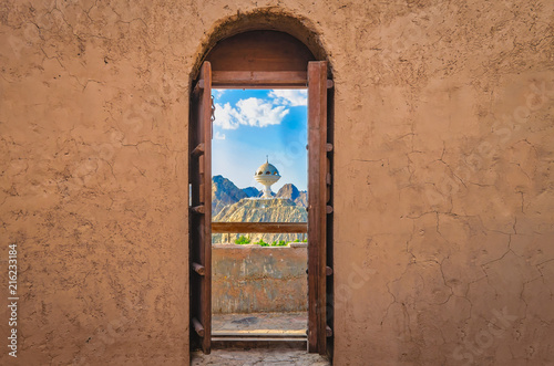 Narrow archway with old, heavy wooden doors opened to show the famous frankincense monument of Muscat, Oman.