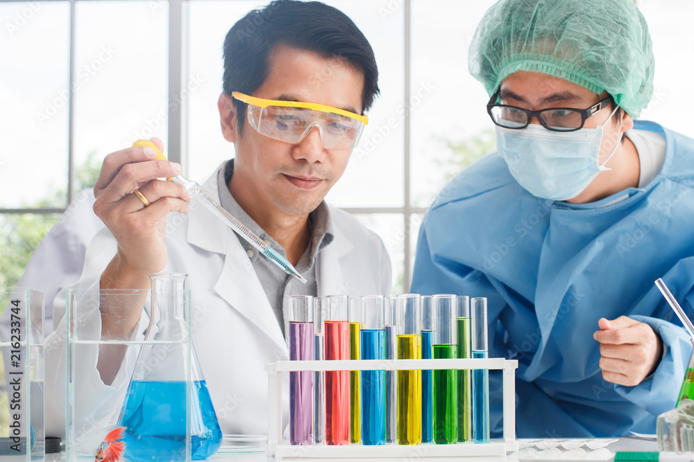 Young male scientist team working with color Glass Measuring Beaker and  color test tube and Siamese fighting fish tank in a laboratory.Concept  Science and Medical image. Stock Photo