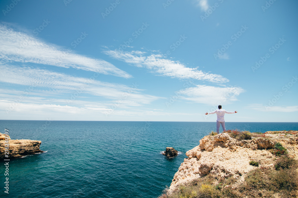 Young man celebrate victory on the edge of cliff on ocean background. Freedom concept.