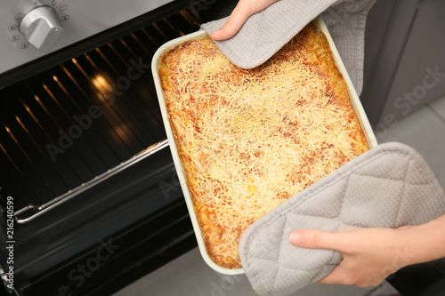 Woman taking baking dish with spinach lasagna out of oven