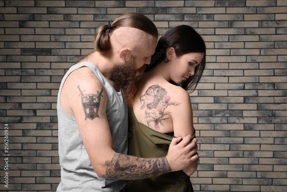 Attractive young couple with tattoos on brick wall background
