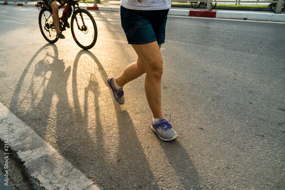 Obraz premium Close-up of sporty woman running on the road in the City park against a beautiful orange sunrise in early morning
