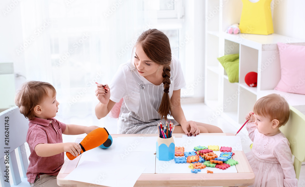 Fototapeta premium Cute little children with young nanny at table, indoors