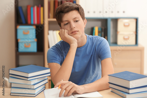 Tired teenager boy doing homework in library