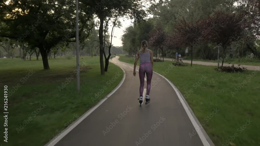 White hansom brown hair girl in tight pants woman riding rollers skates on bike road in parky, summer golden hour White hansom brown hair girl in tight pants woman riding rollers skates on bike road in parky, summer golden hour
