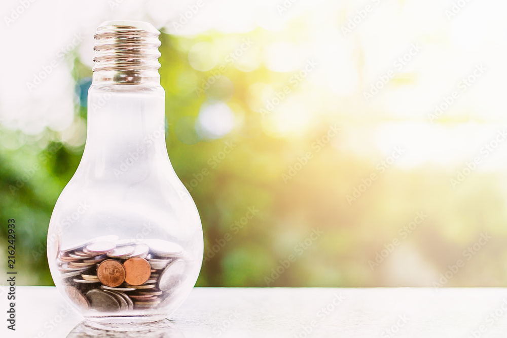 Coins in light bulb bottle shape against blurred natural green background and copy space for investment, business, finance and saving money concept Coins in light bulb bottle shape against blurred natural green background and copy space for investment, business, finance and saving money concept