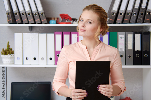 Portrait of a beautiful business blonde girl standing in the office with a folder. photo