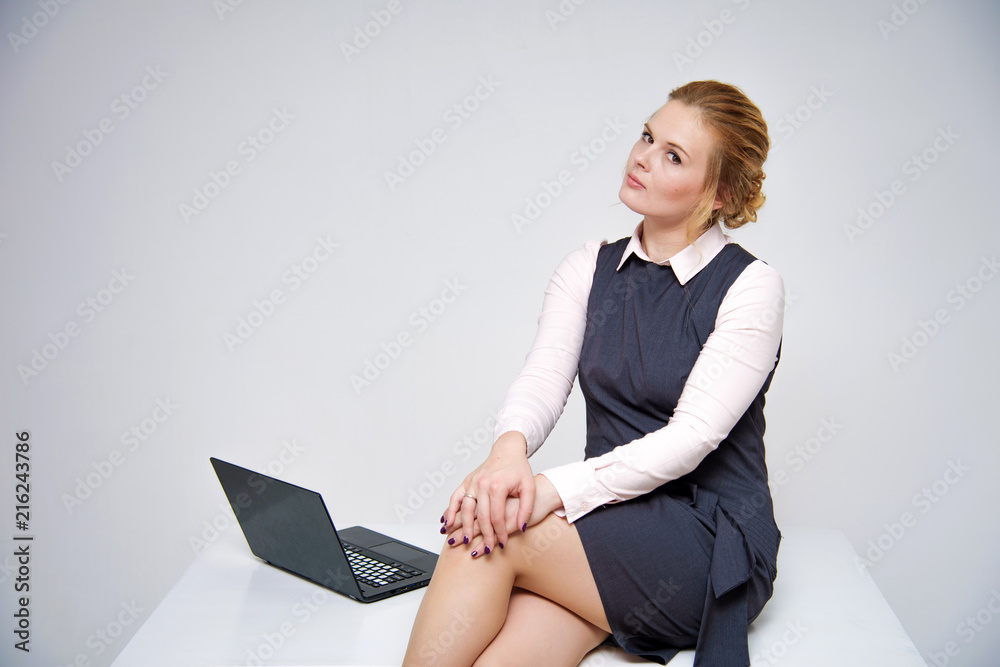 Naklejka premium Portrait of a beautiful blond business girl sitting at desk on white background with laptop.