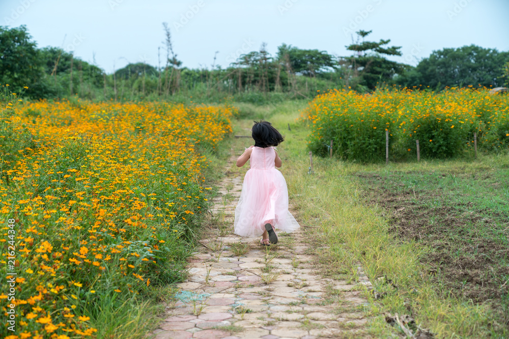 Little girl wearing pink skirt running on daisy flower field