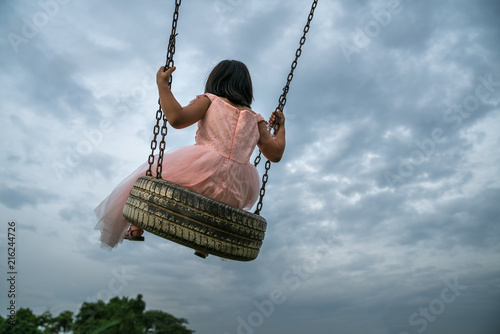 Little girl with skirt play swing at outdoor park. Dramatic sky
