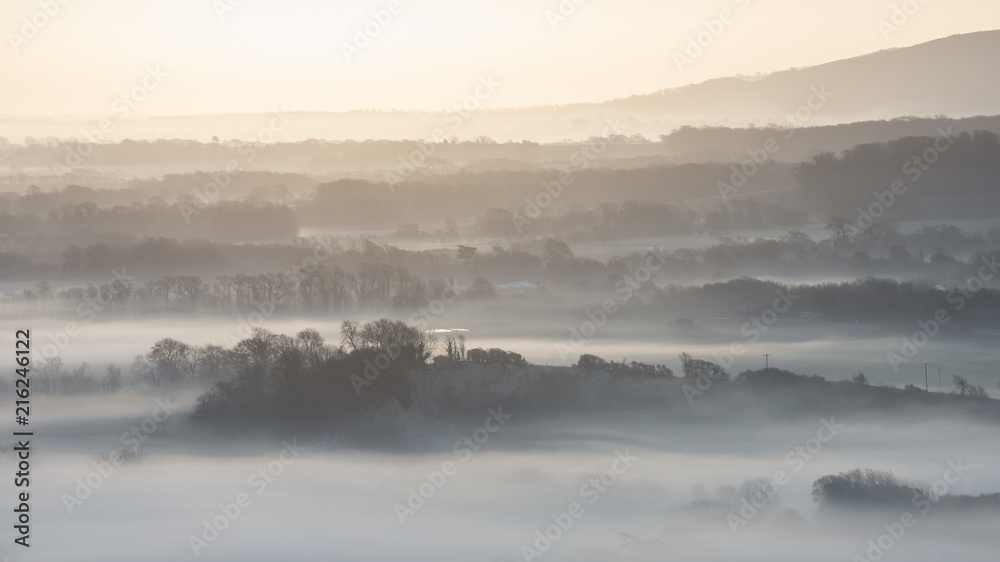 Stunning foggy English rural landscape at sunrise in Winter with layers rolling through the fields