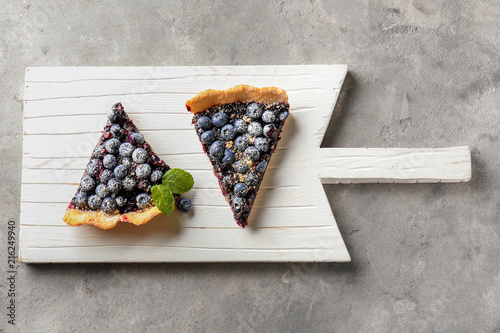 Foto Wooden board with pieces of delicious blueberry pie on table