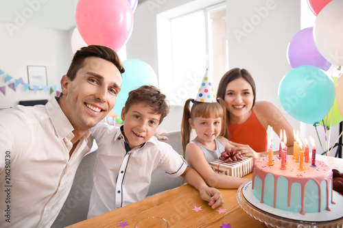 Young man taking selfie with family while celebrating daughter's birthday at home