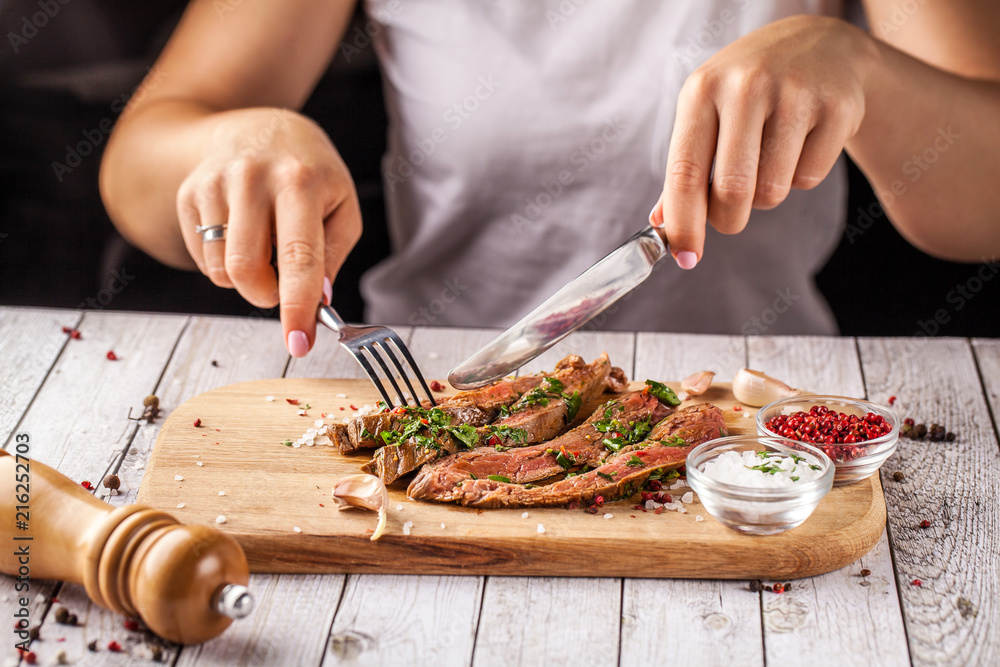 Mexican food. The girl has a fillet of meat steak with the addition of spicy green salsa. meat on a wooden board. Knife and fork in hands. concept of a beautiful dish in a restaurant. selective focus