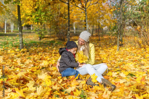 Mother and son sitting in the autumn park among the falling leaves.