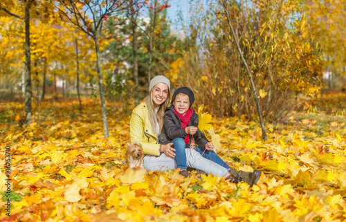Portrait of mother and son sitting in the autumn park among the falling leaves.