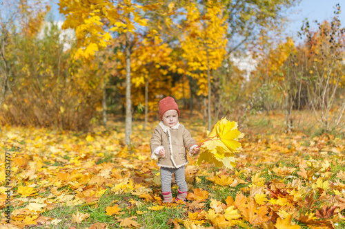 Cute little girl in warm cap with maple leaf play in autumn park.