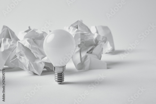 close-up shot of power saving light bulb with crumpled papers on white