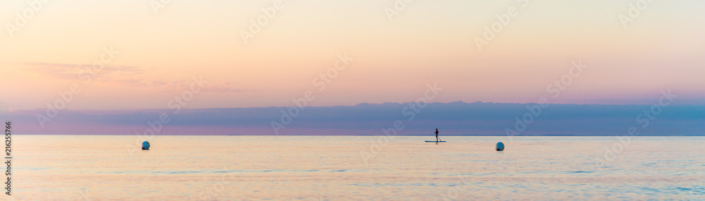 panorama of a quiet scene, single man on Stand Up Paddle Board. SUP. in beatutiful sunset at the beach