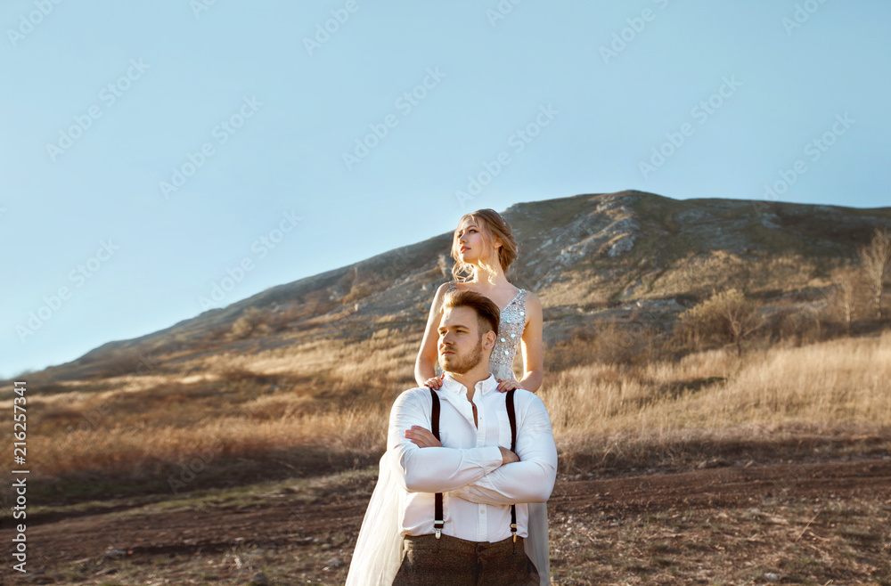 beautiful young couple man and woman standing against the background of a mountain and blue sky in wedding dresses in summer at sunset