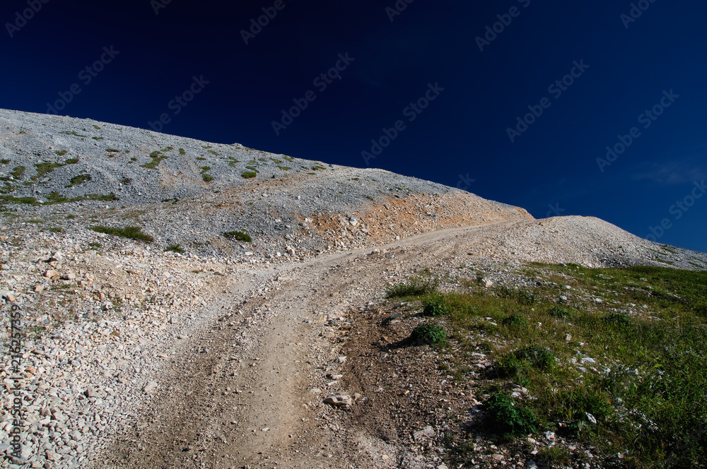 Road path through a white stones rocks on a highland mountains with green grass under blue sky Altai Mountains Siberia Russia