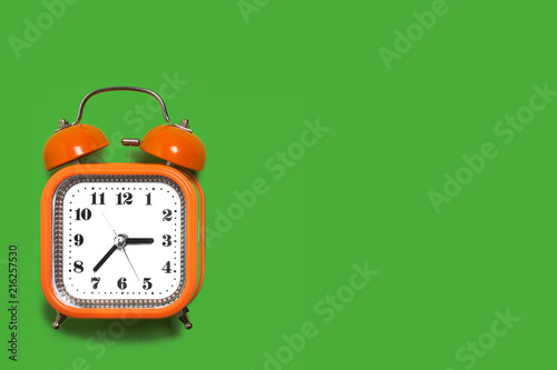 Vintage style orange metal alarm clock with bells standing on the green surface isolated. back to school concept. free space for text
