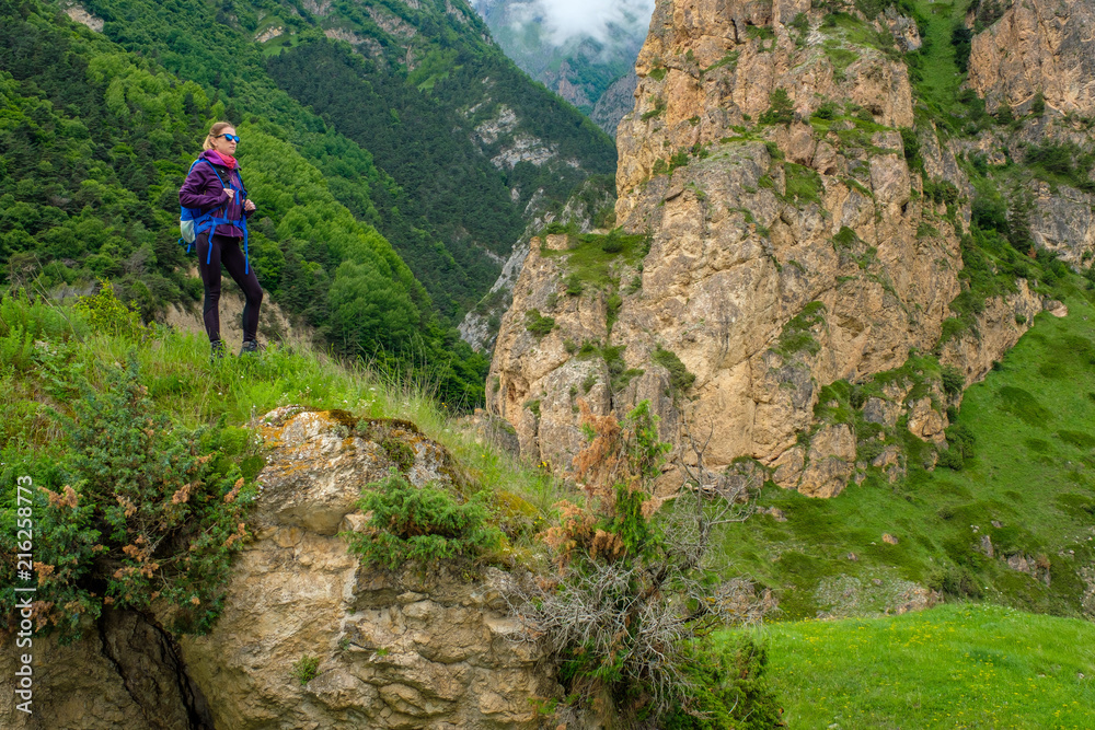 Girl with a backpack in the mountains. Trekking along the mountain road.