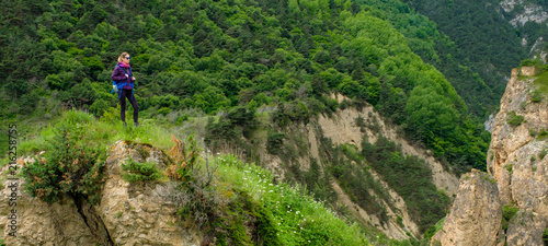 Girl with a backpack in the mountains. Trekking on a mountain road. Panorama of the mountain valley.