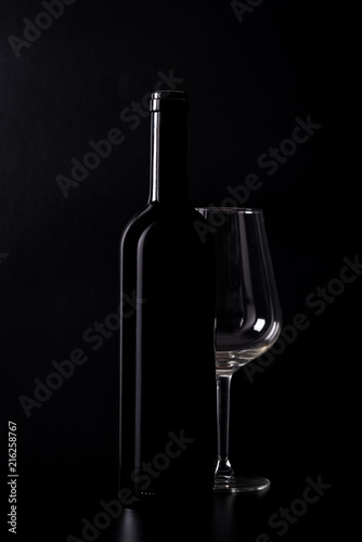Silhouette of red wine bottle with empty half glass isolated on black dark background with soft reflections and beautiful shadows.
