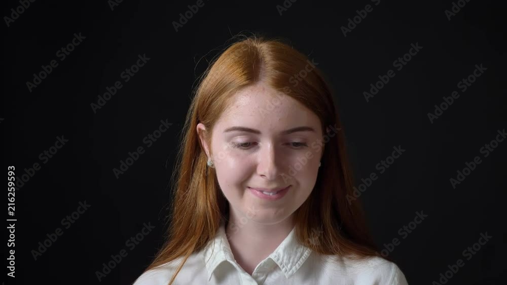 Charming ginger woman touching her hair and smiling at camera, isolated on black background Charming ginger woman touching her hair and smiling at camera, isolated on black background