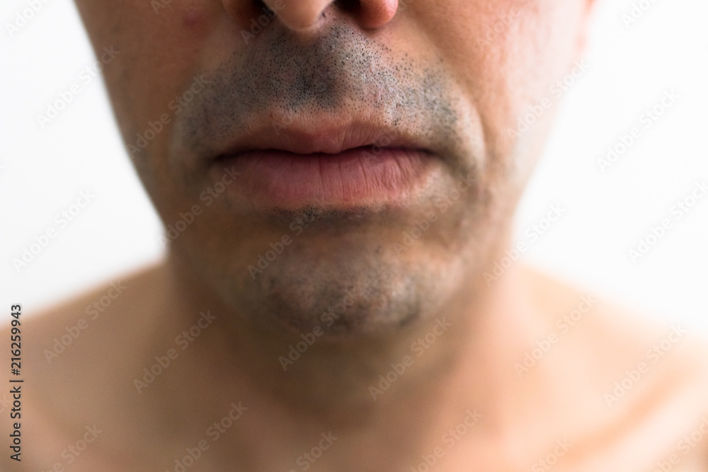 mouth of a man with a shaved beard. detail of the lips in the foreground with blurred white background. lower part of a white man's face