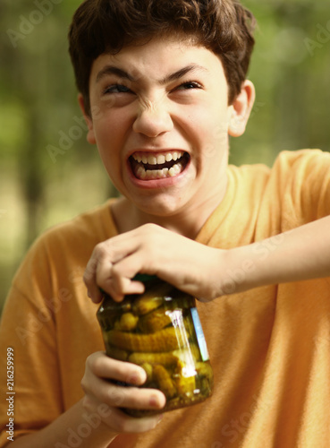 boy with strain grimace try to remove cover from cucumbers jar close up photo