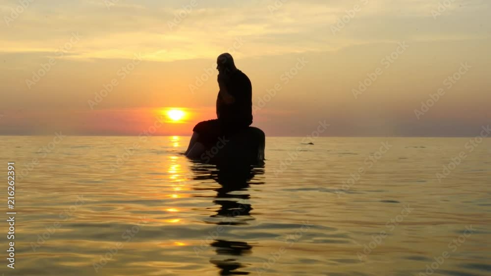 Man on a rock in open sea with mibile phone calling and speaks silhouette