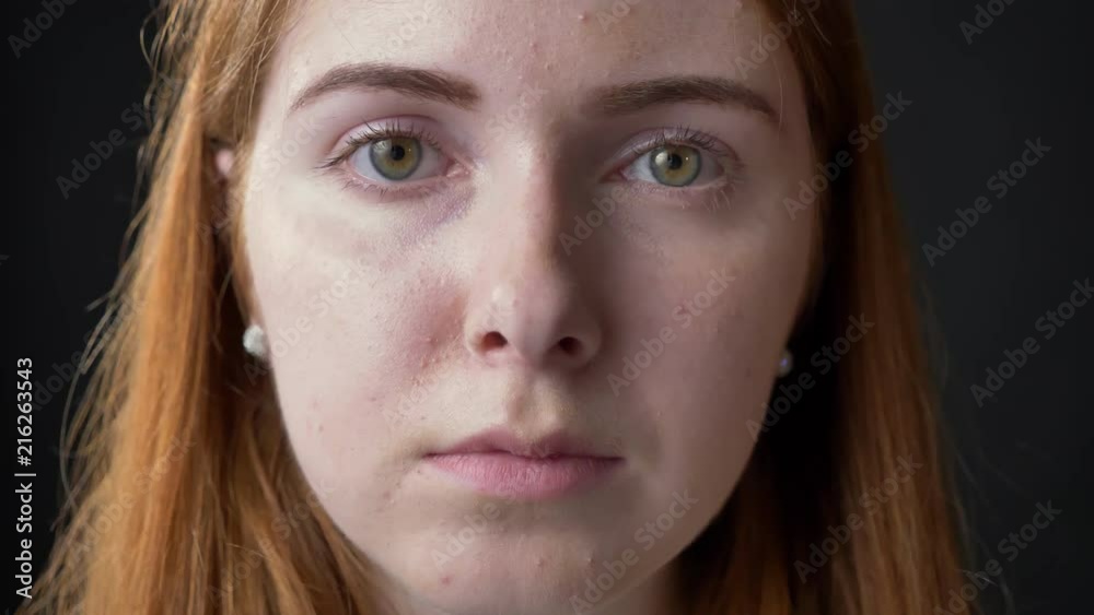 Close portrait of young serious beautiful woman face looking at camera with concerned and occupied expression, black background Close portrait of young serious beautiful woman face looking at camera with concerned and occupied expression, black background