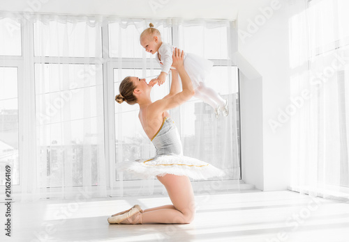 Mother in ballet outfit holding on hands small daughter