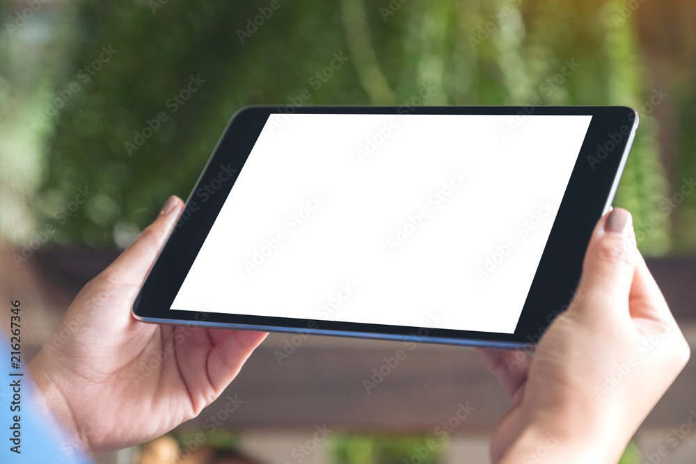 Mockup image of woman holding black tablet pc with white blank desktop screen with green nature background