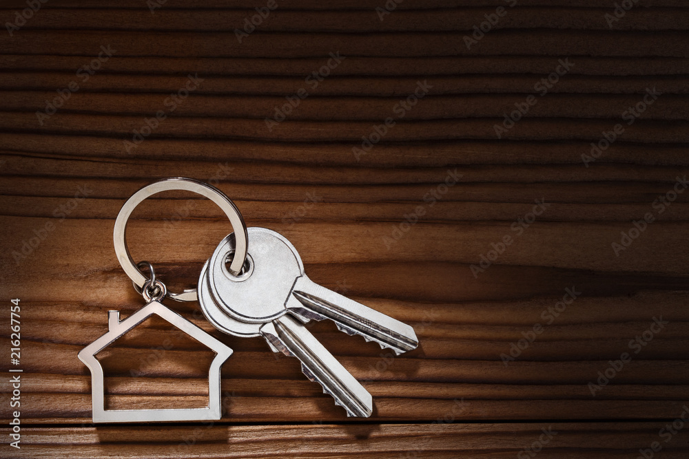 House keys with house shaped keychain on dark wooden background House keys with house shaped keychain on dark wooden background