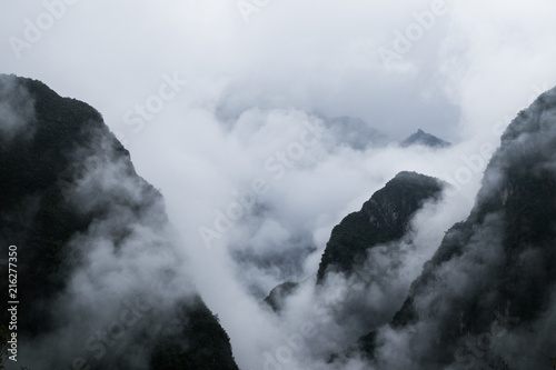 Black mystical mountains appear through thick white clouds. Mysterious gloomy landscape close-up without people