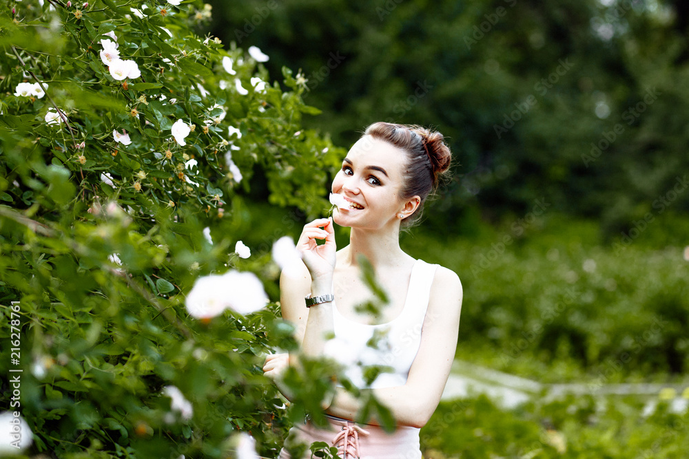 sweet cheerful girl in a white t-shirt and a pink skirt walks in the Park in the summer. She enjoys a walk and holds a flower in her mouth. sweet cheerful girl in a white t-shirt and a pink skirt walks in the Park in the summer. She enjoys a walk and holds a flower in her mouth.