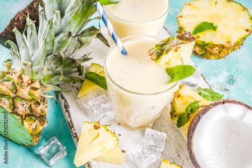 Refreshing summer drink, homemade pina colada cocktail, on a light blue background, with pieces of pineapple, coconut, ice and mint leaves, copy space top view