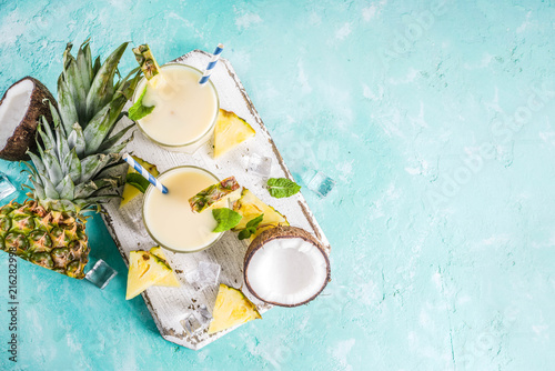 Refreshing summer drink, homemade pina colada cocktail, on a light blue background, with pieces of pineapple, coconut, ice and mint leaves, copy space top view photo