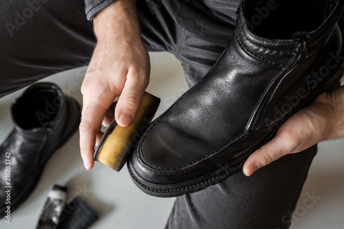 Man's hand applying black cream on elegant leather boots with sponge. Care about boots beauty and protection from cold and wet. Preparing for autumn and winter season. Footwear cleaning concept.