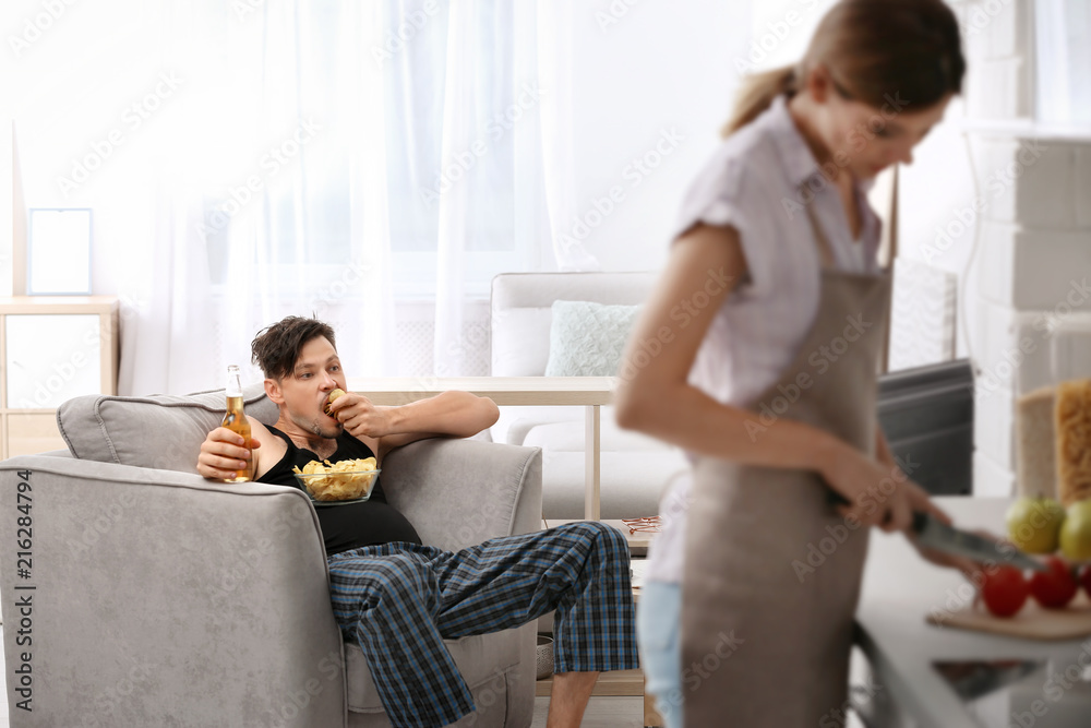 Lazy husband watching TV and his wife cooking at home Stock-foto Adobe Stock