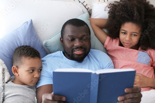 African American man reading bedtime story to his children in bed photo