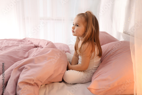 Cute little girl sitting on bed at home