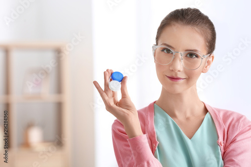 Woman wearing glasses and holding plastic container with contact lenses  indoors